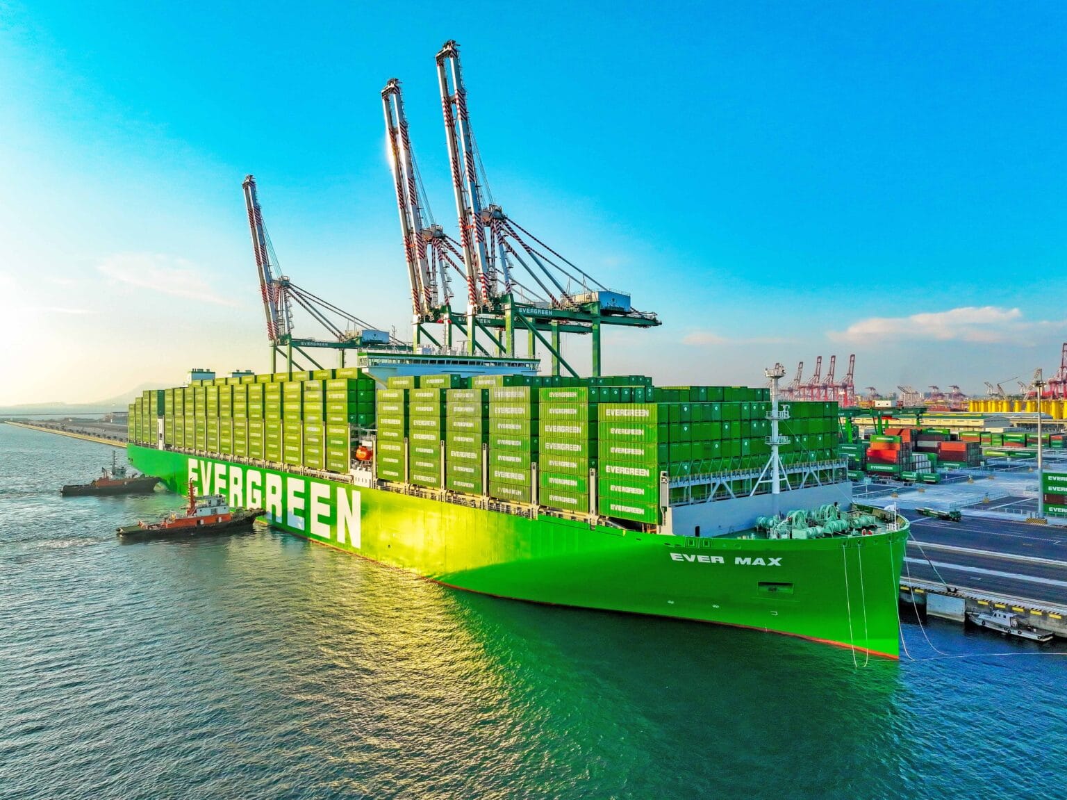 Green container ship Ever Max docked at a port with stacked green cargo containers and large gantry cranes in the background